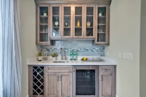 Modern light wood home bar with quartz countertop, glass cabinets, wine storage, and mosaic backsplash.