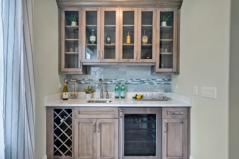 Modern light wood home bar with quartz countertop, glass cabinets, wine storage, and mosaic backsplash.