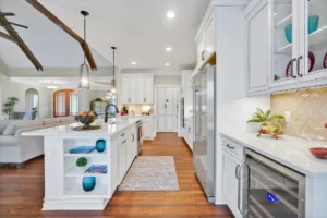 Bright modern white kitchen with wood floors, open layout, island, and stainless steel appliances.