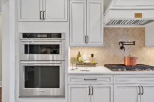 Modern white kitchen with stainless steel appliances, herringbone backsplash, and a copper pot on stove.