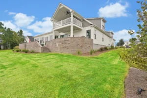 Modern two-story home with white siding, brick terrace, and lush green lawn under blue sky.