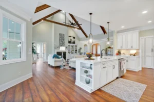 Open-concept modern farmhouse kitchen and living room with vaulted ceilings, wood beams, and white cabinetry.