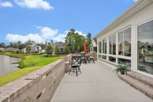 Modern lakeside patio with tables, clubhouse windows, and scenic water view under blue sky.