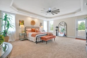 Modern bedroom with tray ceiling, black metal bed, orange accents, and cozy natural lighting.
