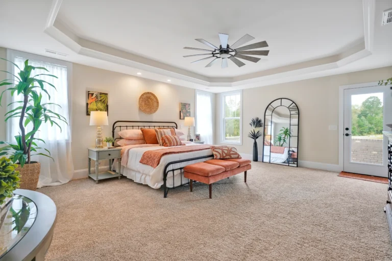Modern bedroom with tray ceiling, black metal bed, orange accents, and cozy natural lighting.