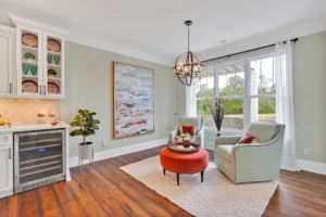 Modern cozy sitting area with gray-blue chairs, orange ottoman, natural light, and elegant decor.