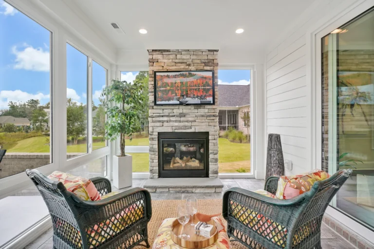 Bright sunroom with stone fireplace, wicker chairs, and large windows filled with natural light.