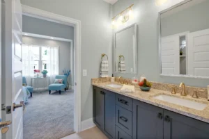 Modern bathroom with double vanity, gold fixtures, granite countertop, and connected light-filled bedroom.