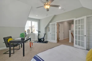 Modern cozy bedroom with workspace, exercise bike, and natural light for comfort and productivity.