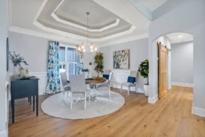 Modern dining room with coffered ceiling, round table, chandelier, and light wood flooring.