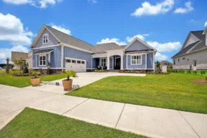 Modern blue suburban house with white trim, front porch, and garage under sunny sky.