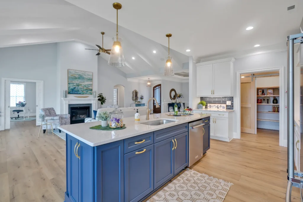 Modern coastal kitchen with blue island, white cabinets, gold lighting, and open living space.