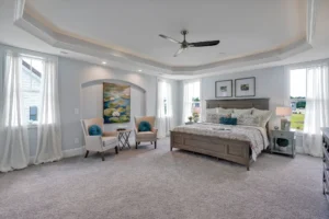 Spacious modern bedroom with neutral tones, elegant decor, tray ceiling, and cozy seating area.