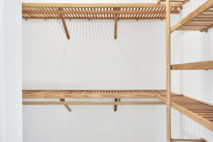 Bright modern closet with white walls and natural wood slatted shelving for stylish organized storage.