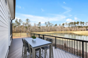 Modern gray deck with outdoor dining overlooking peaceful pond and pine trees under clear skies.