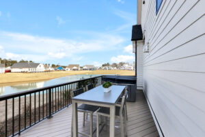 Modern balcony deck with gray seating, light wood flooring, and peaceful waterfront suburban view.