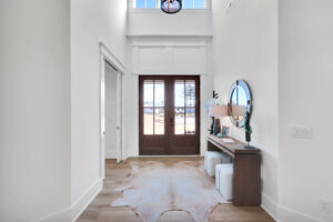 Modern farmhouse entryway with wooden double doors, light floors, cowhide rug, and rustic decor.