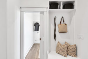 Bright white modern mudroom with built-in bench, striped pillows, wicker baskets, and tan handbag.