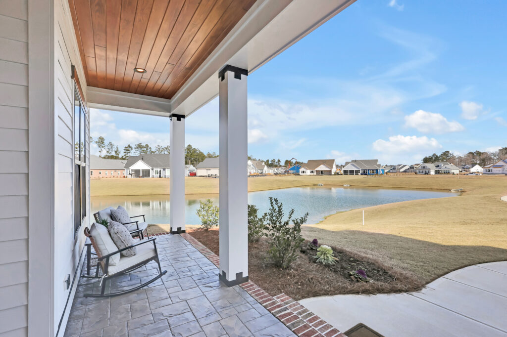 Covered front porch with rocking chairs overlooking pond and suburban neighborhood scenery.