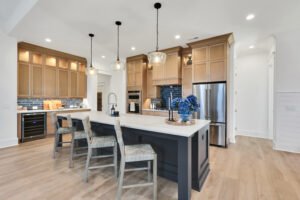 Modern kitchen with navy island, warm wood cabinets, stainless steel appliances, and pendant lighting.