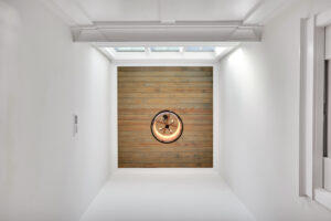 Minimalist hallway with wooden ceiling, warm circular light, and natural skylight illumination.