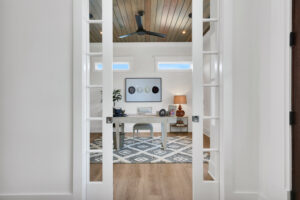 Bright modern home office with French doors, white desk, geometric rug, and wood ceiling.