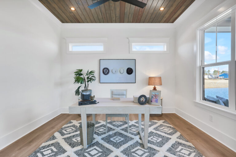 Bright minimalist home office with wood ceiling, white desk, and large sunlit windows.