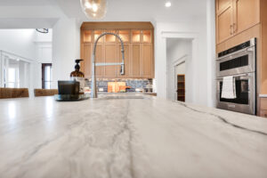 Modern kitchen with marble island, light wood cabinets, stainless steel appliances, and warm ambient lighting.