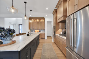 Modern kitchen with wood cabinets, quartz island, pendant lighting, and stainless steel refrigerator.