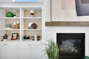 Modern living room with white built-in shelves, black fireplace, wooden mantel, and green plant.