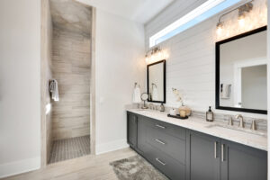 Modern bathroom with double vanity, gray cabinets, marble countertops, and walk-in shower.