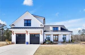 Modern white farmhouse with black trim, metal roof, wooden doors, and spacious front lawn.
