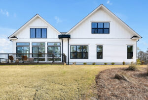 Modern white farmhouse with black trim, large windows, and wooden deck under clear blue sky.