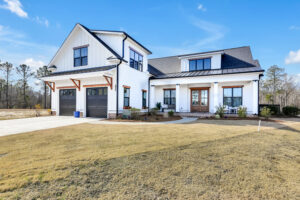 Modern white farmhouse with black trim, wood accents, and covered porch under clear blue sky.