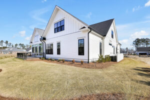Modern white farmhouse with black trim, gable roof, and neat lawn under blue sky.