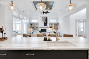 Bright modern open kitchen and living room with marble island, gold faucet, and fireplace.