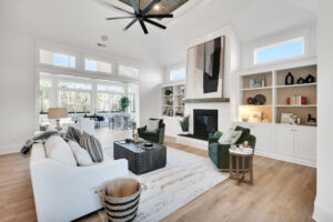 Bright modern living room with vaulted ceilings, green chairs, white sofa, and black fireplace.
