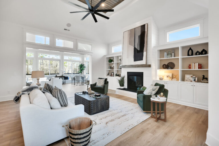 Bright modern living room with vaulted ceilings, green chairs, white sofa, and black fireplace.