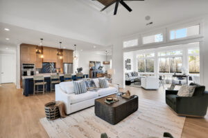Bright modern open-concept living space with white sofa, wood kitchen, island, and large windows.