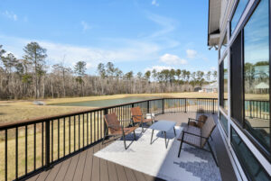 Modern lakeside deck with wicker furniture overlooking pond and trees under a clear blue sky.