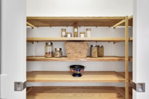Minimalist wooden pantry shelves with glass jars, wicker basket, and decorative kitchen accents.