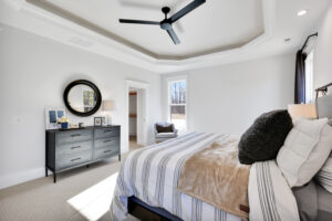 Modern neutral bedroom with layered bedding, black ceiling fan, dark dresser, and elegant decor.