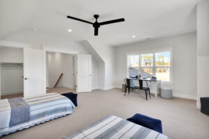 Modern twin bedroom with striped bedding, beige carpet, black ceiling fan, and bright workspace.