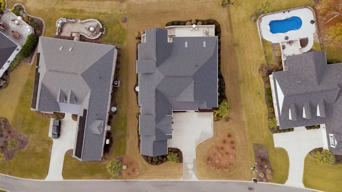5 Mistakes to Avoid When Buying a Lot 1 : Aerial top-down view of suburban luxury homes with custom roofs, driveways, landscaped yards, and a swimming pool.