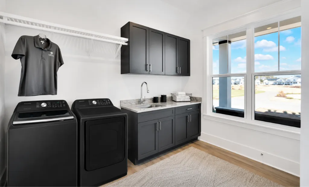 Modern laundry room featuring matte black appliances, dark gray cabinets, a sink, and a bright window.